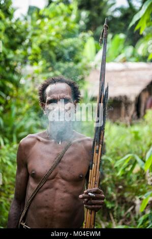 Das autonomiegesetz von einem Korowai Stamm. Korowai kombai (Kolufo) mit Bogen und Pfeile, die auf den natürlichen Wald Hintergrund Stockfoto