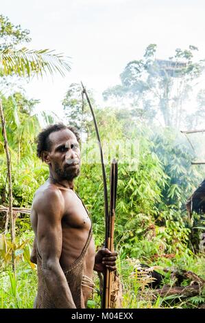 Das autonomiegesetz von einem Korowai Stamm. Korowai kombai (Kolufo) mit Bogen und Pfeile, die auf den natürlichen Wald Hintergrund Stockfoto