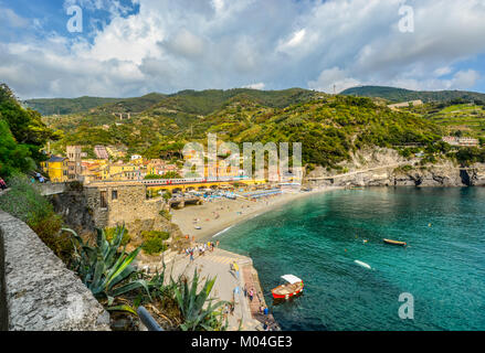 Der Sandstrand Spiaggia di Fegina, der Bahnhof mit Zügen läuft, die Berge, das Meer und bunten Dorf Monterosso, Cinque Terre Italien Stockfoto