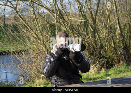 Professioneller männlicher Naturfotograf, der am kalten Wintermorgen in Großbritannien fotografiert. Stockfoto
