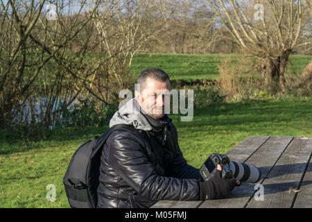 Professionelle natur Fotograf ruht seine Canon Kamera auf Picknick Tisch und nimmt einen Bruch von Aufnahmen im Park an einem kalten Wintermorgen. Stockfoto