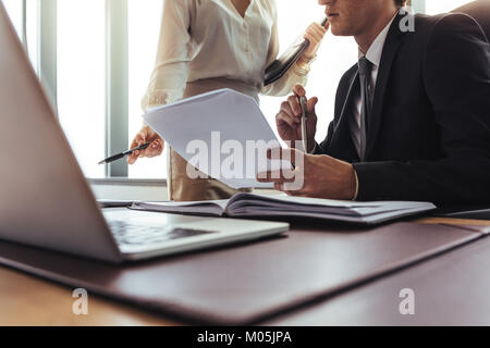 Nahaufnahme von Geschäftskollegen, die Dokumente im Büro lesen und vergleichen. Geschäftsmann sitzt am Schreibtisch und hält Vertragspapiere mit weiblicher Kollegin p Stockfoto