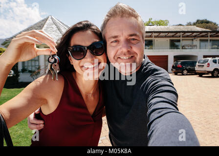 Glückliches Paar mit Tasten außerhalb neues Zuhause und nehmen eine selfie. Mann, ein Selbstportrait mit Frau mit einem neuen Ihrer neuen Immobilie. Stockfoto