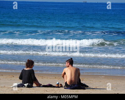 Zwei Freunde sitzen am Strand Sand auf einem perfekt klaren Tag und ein Gespräch mit jeder anderen Stockfoto