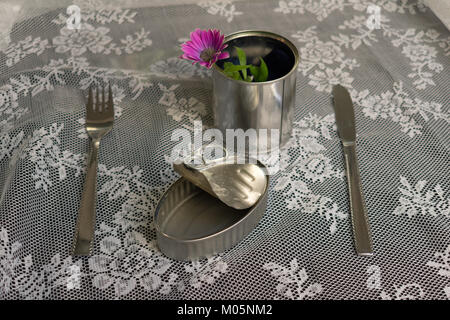 Leere sardine Blechdose mit nichts zusammen zu einer Gabel, Messer und Pot mit einem lila Blumen und grüne Blätter auf der Seite auf weißem Hintergrund Essen Stockfoto