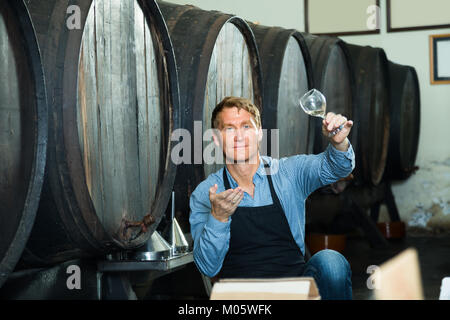 Professionelle Winzer holding Glas Wein aus Holz Barrel im Weinkeller gegossen Stockfoto