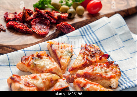 Runde Sausage Pizza Margherita mit Stücken auf eine Serviette mit getrockneten Tomaten und Kräuter Thymian und Rosmarin. Selektive konzentrieren. Die horizontalen Rahmen. Stockfoto