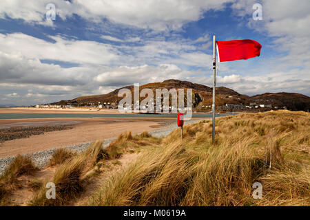 Sanddünen und rote Flagge in Fairbourne auf dem Wels Küste, mit der Küstenstadt Barmouth im Hintergrund Stockfoto