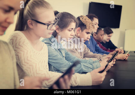 Positive europäische Mitschüler über ihre Smartphones intensiv während der Klassen Stockfoto