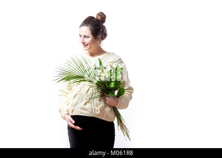 Eine junge schöne Frau in einem gestrickten Pullover und einem schwarzen Kleid auf Ihrem letzten Schwangerschaft hält einen Strauß Blumen von Blenden in die Hände und lächelt auf ein Stockfoto