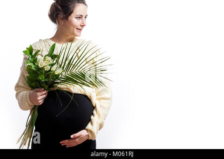 Junge fröhliche dunkelhaarige Frau in Form gestrickter Pullover und schwarzes Kleid auf der späten Schwangerschaft hält einen Strauß Blumen und lächelnd auf Weiß isoliert backgro Stockfoto