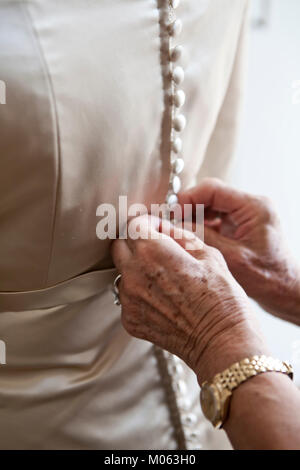Hände von einer alten Frau knopfverschluß das Kleid der Braut Stockfoto