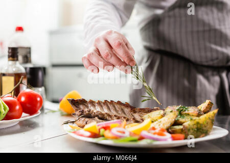 Mit einem Zweig Rosmarin eingerichtet. bereitet der Küchenchef im Restaurant. Gegrillter Lammrücken mit Bratkartoffeln und frischem Gemüse Stockfoto