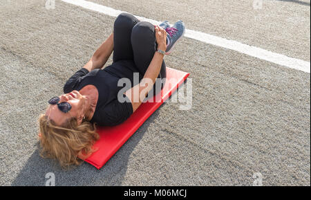 Model Released - ältere Frau (70-75) Stretching auf Matte zum Fitnessbereich im Freien Stockfoto