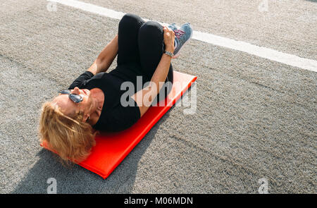 Model Released - ältere Frau (70-75) Stretching auf Matte zum Fitnessbereich im Freien Stockfoto