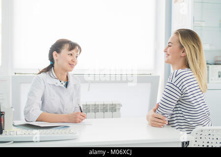 Patienten erhalten eine ärztliche Konsultation und Blick in die Kamera Lächeln, sitzt die Ärztin am Schreibtisch Hintergrund auf Stockfoto