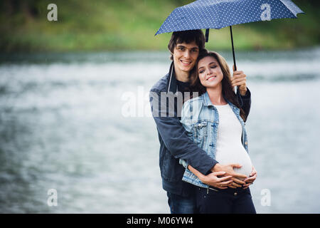 Schwangere Frau und Mann hält ein Regenschirm im Park in der verregneten Tag im Freien. Stockfoto