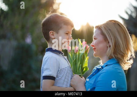 Wenig Sohn schenkt Blumenstrauß aus Tulpen am Muttertag im Sonnenuntergang zu Mama, miteinander suchen Stockfoto