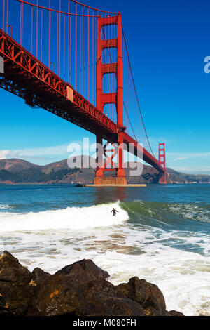 Golden Gate Bridge Surfer reitet eine Welle unter dem Span in Richtung der felsigen findlingen an der Unterseite der Brücke Stockfoto