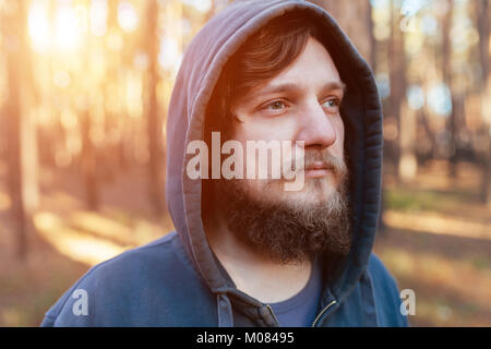 Nahaufnahme Portrait eines bärtigen hipster Tourist in graue Motorhaube Mann im Sonnenlicht Wald Stockfoto