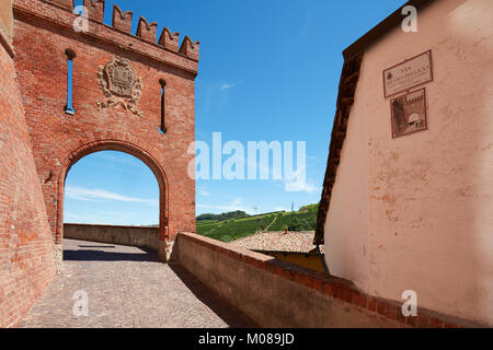 Barolo mittelalterlichen Burg Eingang arch in roten Ziegeln und Emblem mit leere Straße und grünen Hügel auf einem sonnigen Sommertag Stockfoto