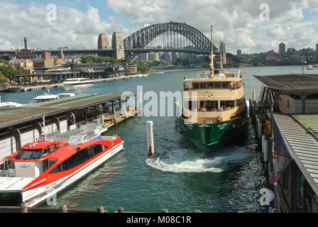 Circular Quay mit Fähren Docking und der Sydney Harbour mit Sydnay Harbour Bridge im Hintergrund. Frühjahr/Tag Sommer, sonnig, blauer Himmel, flauschige Wolken. Stockfoto