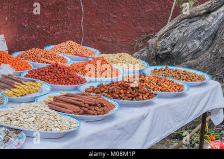 Tabelle mit einer weißen Tischdecke, ein Sortiment von bunten Essbares auf Platten, und eine tiefe rote Wand im Hintergrund, in San Miguel de Allende Stockfoto