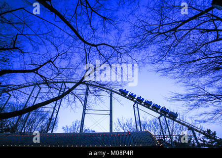 Weitwinkelaufnahme einer Achterbahnfahrt in einem Vergnügungspark mit Niederlassungen und blauer Himmel. Ein wenig Lärm und Korn. Stockfoto