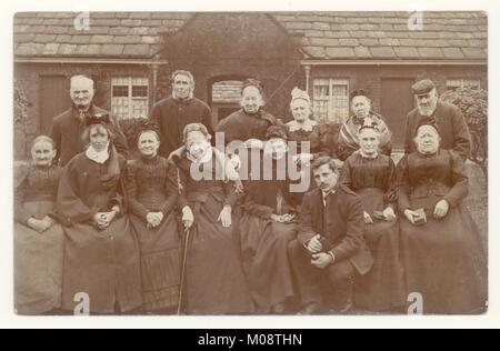 Edwardian Postkarte group Portrait von älteren Frauen und Männern außerhalb ein armenhaus oder armenhaus (gemeinnützige Wohnungsbau) mit Reverend und Frau, vielleicht mit einem Bibelstudium, Großbritannien, circa 1905. Stockfoto