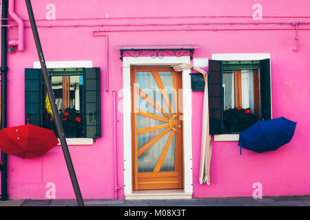 Rosa Haus Wand mit zwei Fenstern und Sonnenschirmen hingen in der Nebensaison in Insel Burano, Venedig, Italien. Stockfoto