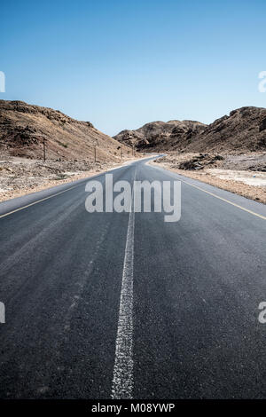 Eine leere Asphaltstraße über dürren Berge im Sultanat Oman im Al Wusta Governate Stockfoto