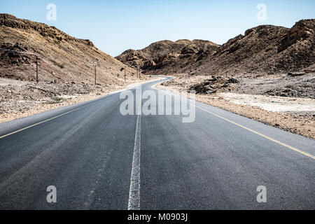 Eine leere Asphaltstraße über dürren Berge im Sultanat Oman im Al Wusta Governate Stockfoto