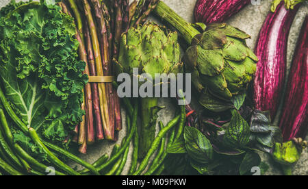 Flachbild-lay von Grün und Violett Gemüse über grauer Beton Hintergrund, Ansicht von oben. Lokalen, saisonalen Produkten für gesundes Kochen. Eggplans, grüne Bohnen, ka Stockfoto
