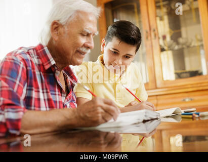 Kleiner Junge macht Schule Hausaufgaben mit alten Menschen zu Hause. Stockfoto