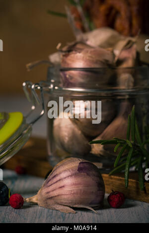 Vertikale Foto von Mehrere Knoblauchzehen. Die Nelken haben dunkle Haut mit violetten Farbton. Gemüse wird in Glas Glas mit Deckel, hat grüne Dichtung platziert Stockfoto