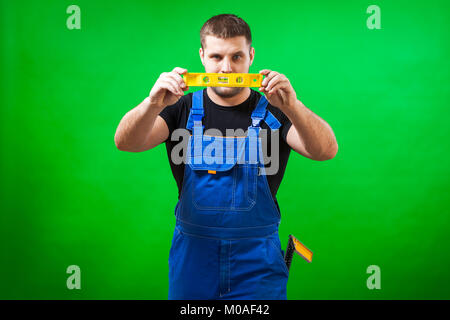 Ein junger Mann builder Arbeiter, der ein schwarzes T-Shirt und Blauen Bau die verwendet, um seltene magnetische Niveau auf einem Grün isoliert Hintergrund Stockfoto