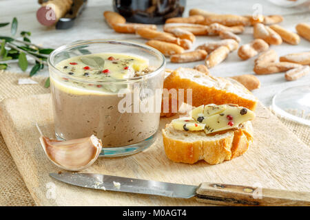 Huhn Leber pate Jar mit zerlassener Butter bedeckt und mit Lorbeerblättern und schwarze und rote Paprika eingerichtet. Stockfoto