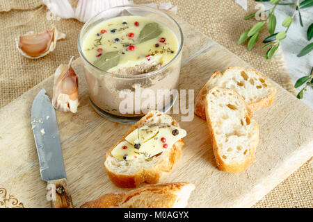 Huhn Leber pate Jar mit zerlassener Butter bedeckt und mit Lorbeerblättern und schwarze und rote Paprika eingerichtet. Stockfoto