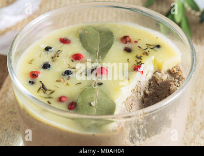 Clos von Huhn Leber pate Jar mit zerlassener Butter bedeckt und mit Lorbeerblättern und schwarze und rote Paprika eingerichtet. Stockfoto