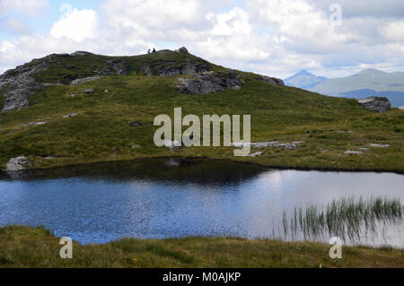 Ein paar Mittagessen in über einem winzigen Lochan auf dem Gipfel des Schottischen Berge Corbett Beinn a Choin in den schottischen Highlands, Großbritannien. Stockfoto