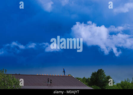 Eine kleine Abbildung des Builder auf der braunen Dach des Hauses, in der Entfernung, vor dem Hintergrund einer schönen, Reichen dramatische Himmel. Stockfoto