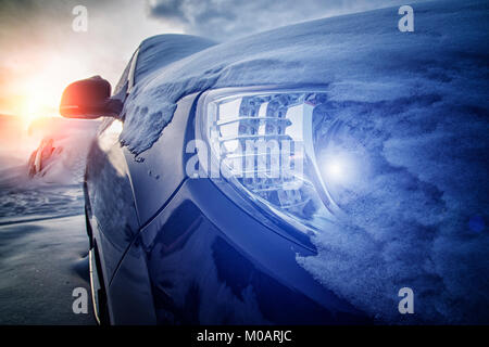 Die Front des Autos mit der Verschneiten Scheinwerfer und den Sonnenuntergang von der Wintersonne im Hintergrund Stockfoto