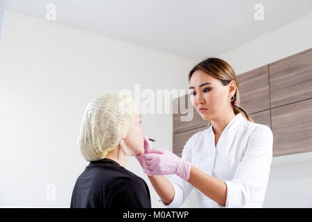 Junge Frau Doktor Kosmetikerin im weißen Kittel und sterile Handschuhe zeichnet eine Markierung auf die Wangenknochen der Frau vor Botox Injektion Formen zu korrigieren. Stockfoto