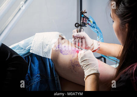 Nahaufnahme der Master tattoo zeichnet die rote Farbe auf den Clients tattoo. Tattoo artist Holding ein Metall Tattoo Maschine in sterile Handschuhe und Arbeiten o Stockfoto