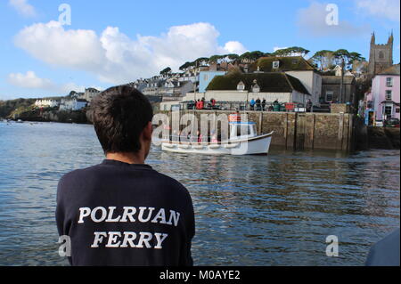 Die Rückseite der Fährmann, der ein schwarzes T-Shirt mit Polruan geschrieben als die Fähre Fowey Harbour und einem kleinen weißen Boot Kreuze vor erreicht. Stockfoto