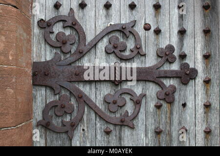 Alte dekorative Scharnier auf einem Verwitterten verzierte Tür neben einer roten Sandstein Mauer bei Kirkmadrine Kirche, Dumfries und Galloway Stockfoto