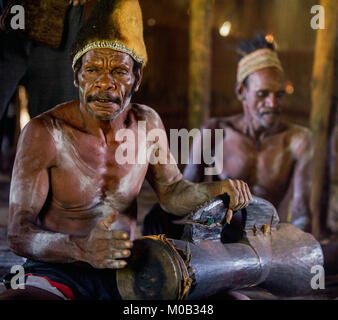 Porträt eines Mannes aus dem Volk der Asmat Menschen mit einer Trommel in der Men's Haus. Asmat Begrüßungszeremonie. Stockfoto