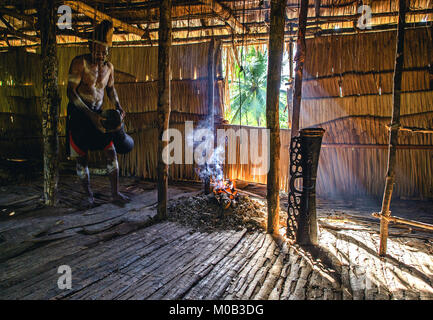 Porträt eines Mannes aus dem Volk der Asmat Menschen mit einer Trommel in der Men's Haus. Asmat Begrüßungszeremonie. Stockfoto