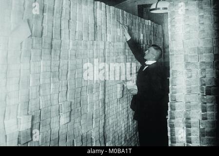 Die Inflation in Weimar Deutschland hat Papiergeld in einer Berliner Bank von Boden bis Decke gestapelt; der Banker zählt Schurken aus gebündelten Banknoten. Stockfoto
