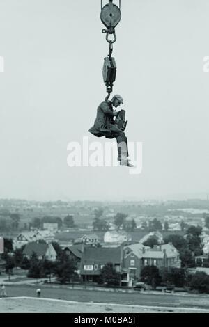 Noch Fotograf hängt ausgesetzt hoch über dem Boden, auf den Haken eines großen Kran. Stockfoto